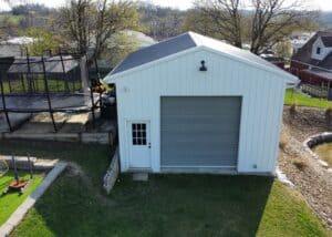 White metal garage with a roll-up door and side door, surrounded by a backyard with a trampoline and soccer goal.