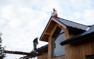 2149343678-min Two workers installing metal roofing on a wooden house in Pittsburgh.