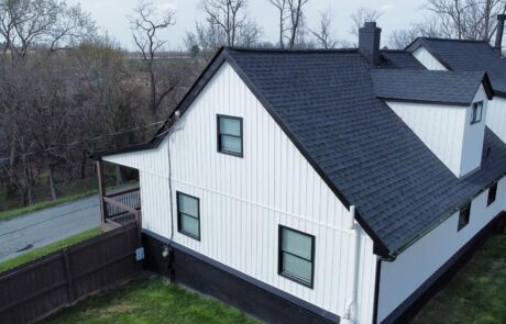 dji_fly_20250414_164636_557_1745076595103_photo_optimized (1) A white house with black roofing and a small porch in a residential neighborhood.
