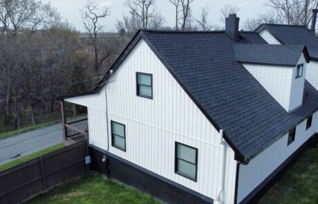 dji_fly_20250414_164636_557_1745076595103_photo_optimized (2) (1) White house with black roofing shingles and a small porch in a suburban area.