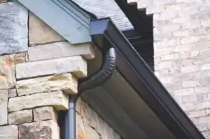 gutters_1769534035170-BBuxA1Zf Close-up of a black gutter and downspout on a stone house exterior.