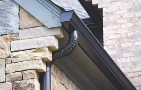 gutters_1769534035170-BBuxA1Zf Close-up of a black gutter and downspout on a stone house exterior.